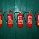 four fire extinguishers lined up against a green wall